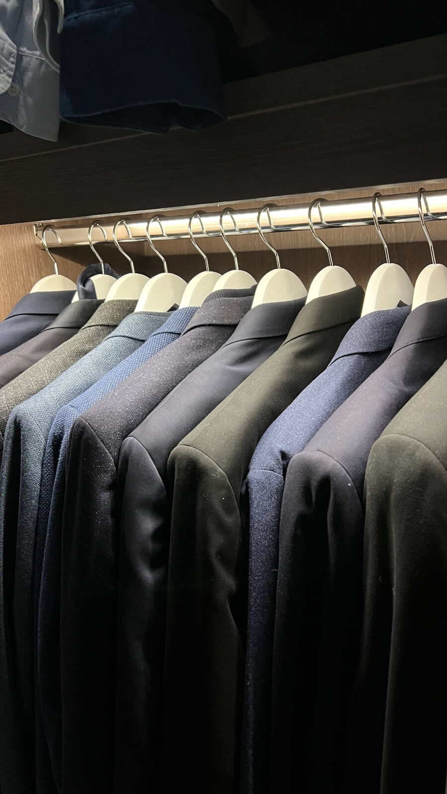 A row of jackets on white wooden hangers along a lit wardrobe rail