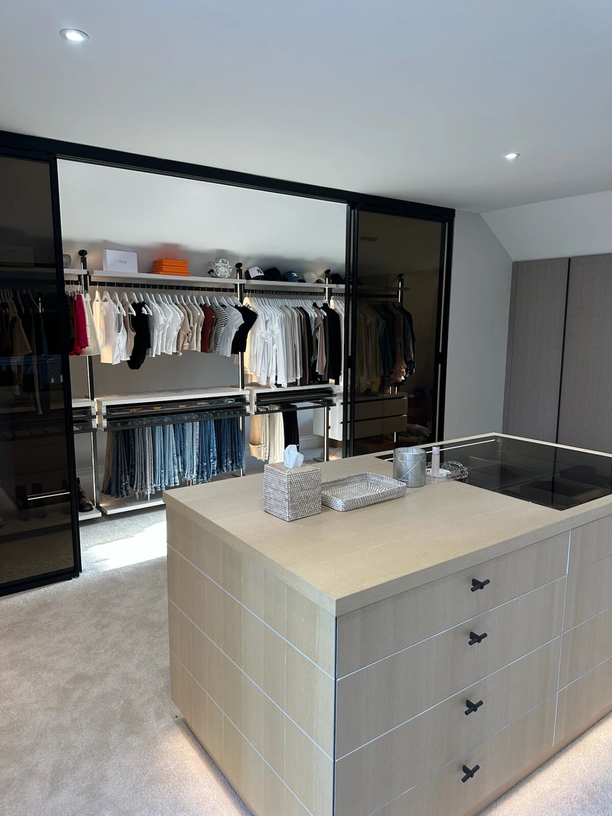 A newly fitted dressing room we organised, with clothes hung behind glass doors and a central island of drawers