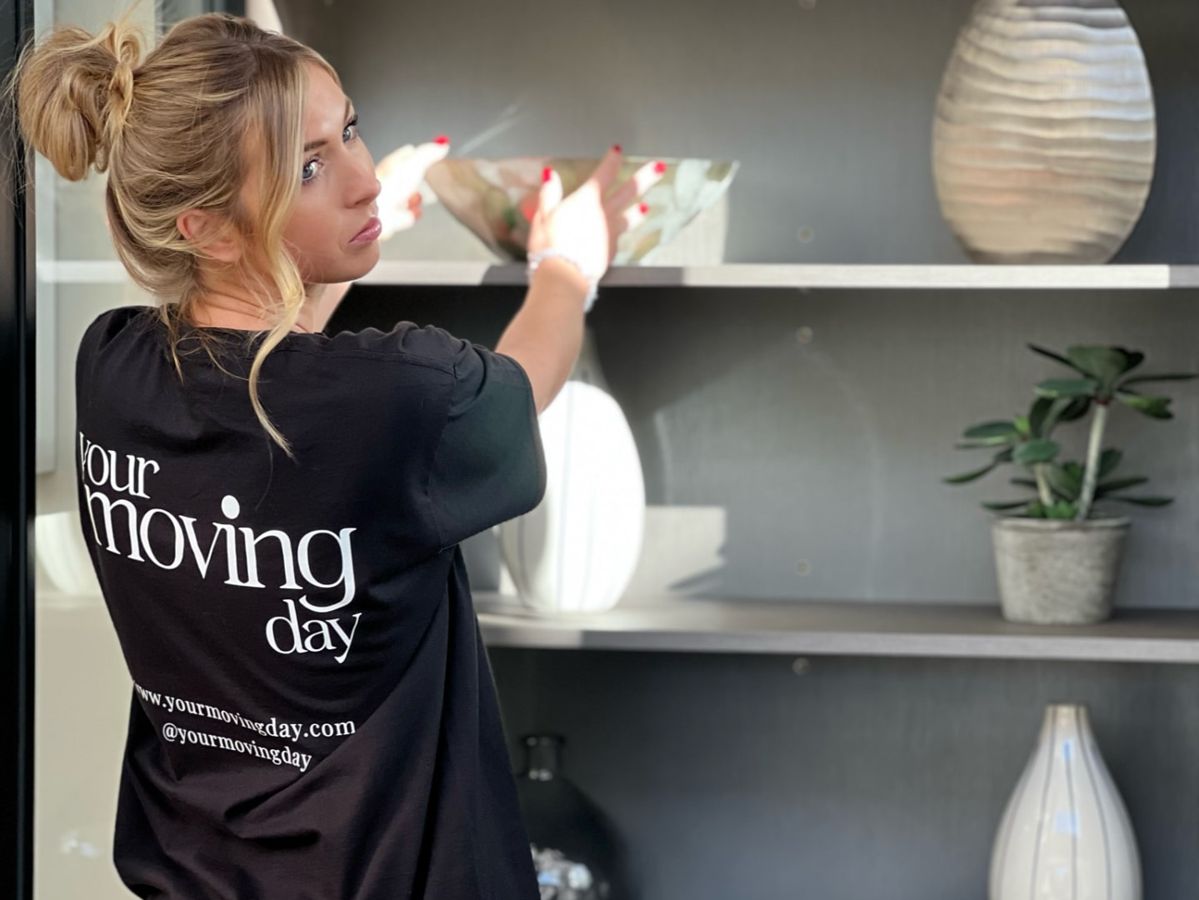 A Your Moving Day organiser in a branded T-shirt arranging a glass bowl and vases on a client’s shelves