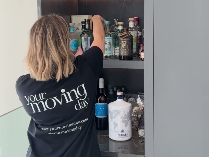 A Your Moving Day organiser arranging bottles on the lit shelves of a drinks cabinet during the Sunningdale unpack